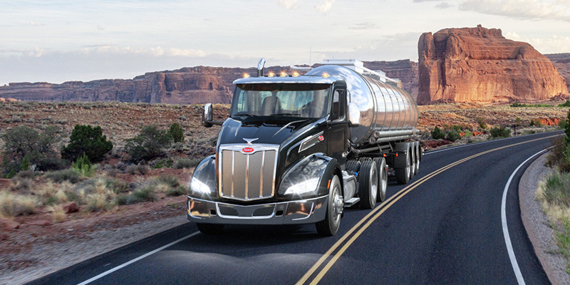 Peterbilt day cab with a tank trailer driving through a desert with rock formations in the background.
