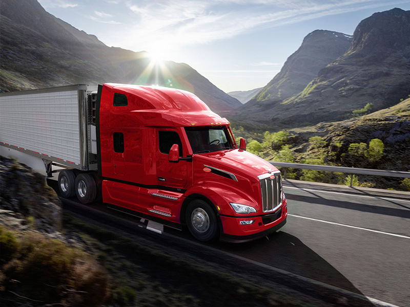 Red Peterbilt 579 Semi-Truck Driving down a mountain road in the sunshine