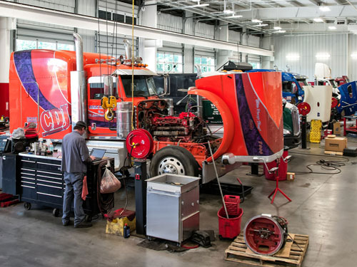Orange Peterbilt 389 being serviced by a Pete Store Diesel Technician